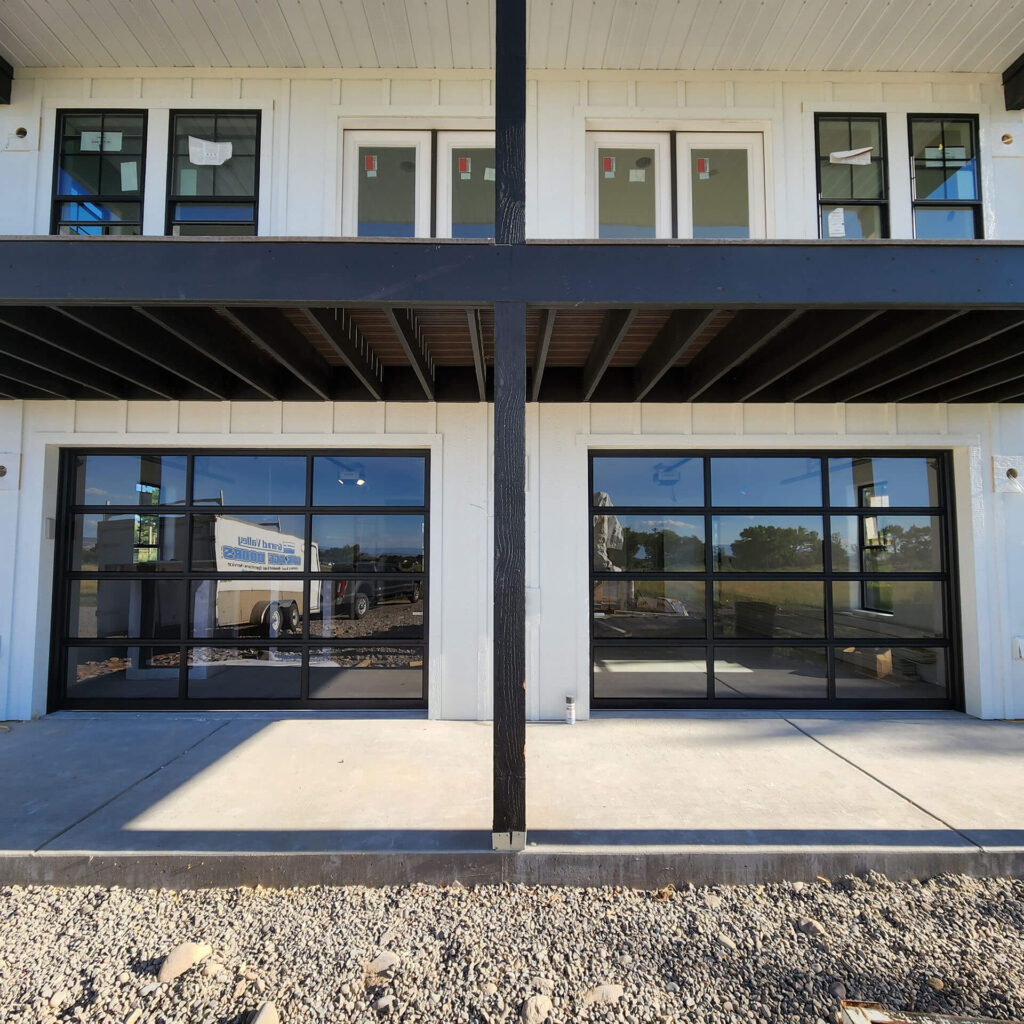 A two-story building near me boasts sleek glass garage doors on the lower level and multiple windows above. The ground out front is neatly covered with gravel.