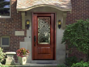 A charming wooden front door with an ornate glass panel, flanked by two lanterns, graces this nearby brick house, complemented by lush greenery and a potted plant on the left.