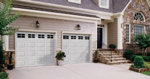 A suburban house with two white garage doors, stone facade accents, front steps, and neatly trimmed greenery.