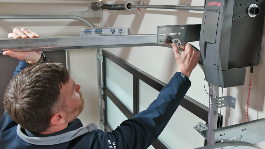 A person installs a garage door opener, adjusting the rail and using a level to ensure alignment.