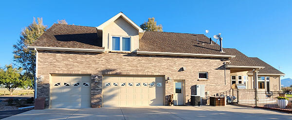 Two-story suburban house with brick exterior, three-car garage, multiple windows, and a paved driveway on a clear day.