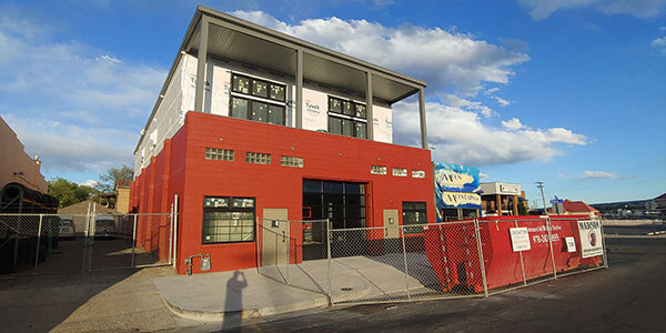 A two-story commercial building with a red lower facade and white upper facade, surrounded by a chain-link fence, under a partly cloudy sky.
