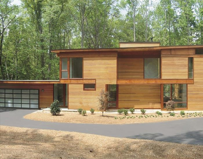 Wooden modern home surrounded by trees and driveway.